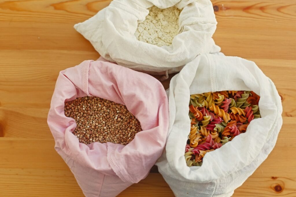 Groceries in reusable textile bags on wooden table, top view